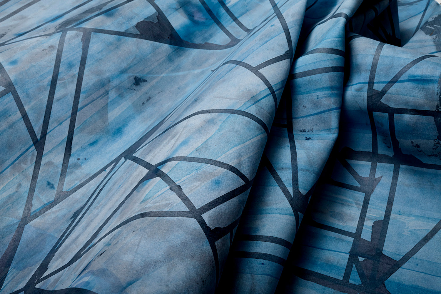 Close-up of a draped cowhide rug in mottled blue and navy with a geometric black overlay.