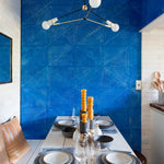 A kitchen table set with dishes against an Installation of leather wall tiles in an angular geometric pattern in blue and white.