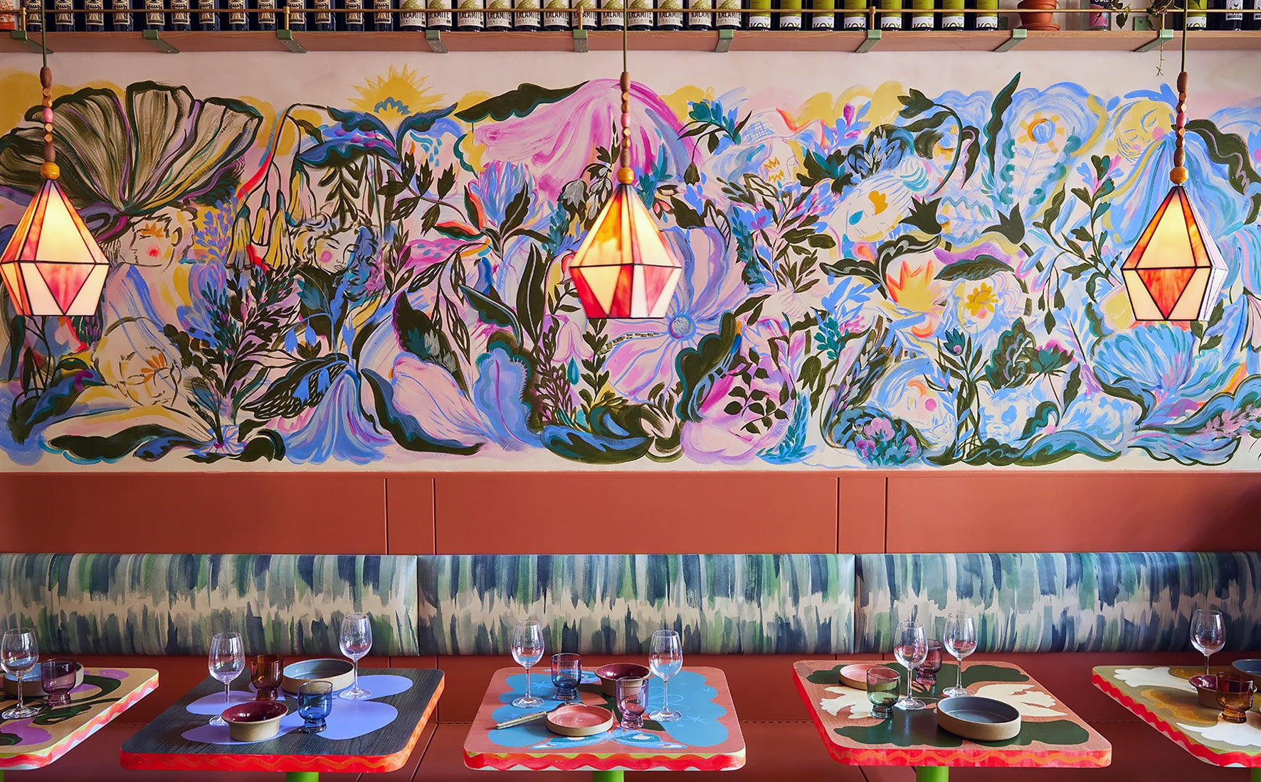 A row of colorful restaurant booths with a painted mural and cushions upholstered in painted leather.