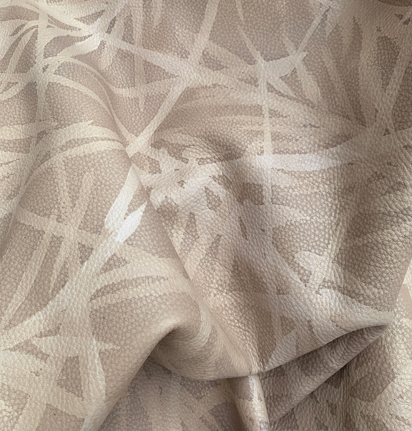 Close-up of a draped cowhide rug in tan with a painterly botanical overlay in cream.