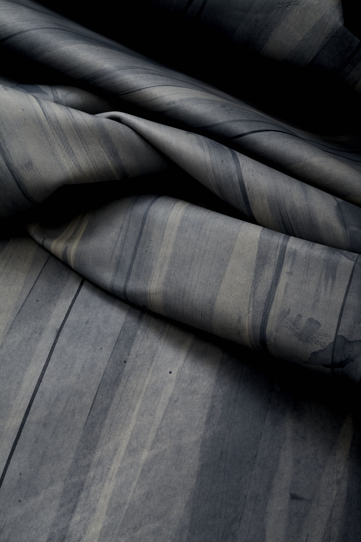 Draped upholstery leather in blue with an abstract stripe overlay in shades of navy and gray.