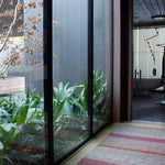 An airy hallway with floor-to-ceiling windows and a woven leather floor rug in shades of purple and pink.