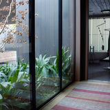 An airy hallway with floor-to-ceiling windows and a woven leather floor rug in shades of purple and pink.