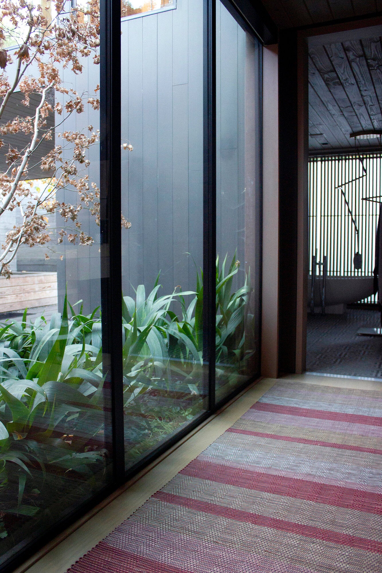 An airy hallway with floor-to-ceiling windows and a woven leather floor rug in shades of purple and pink.