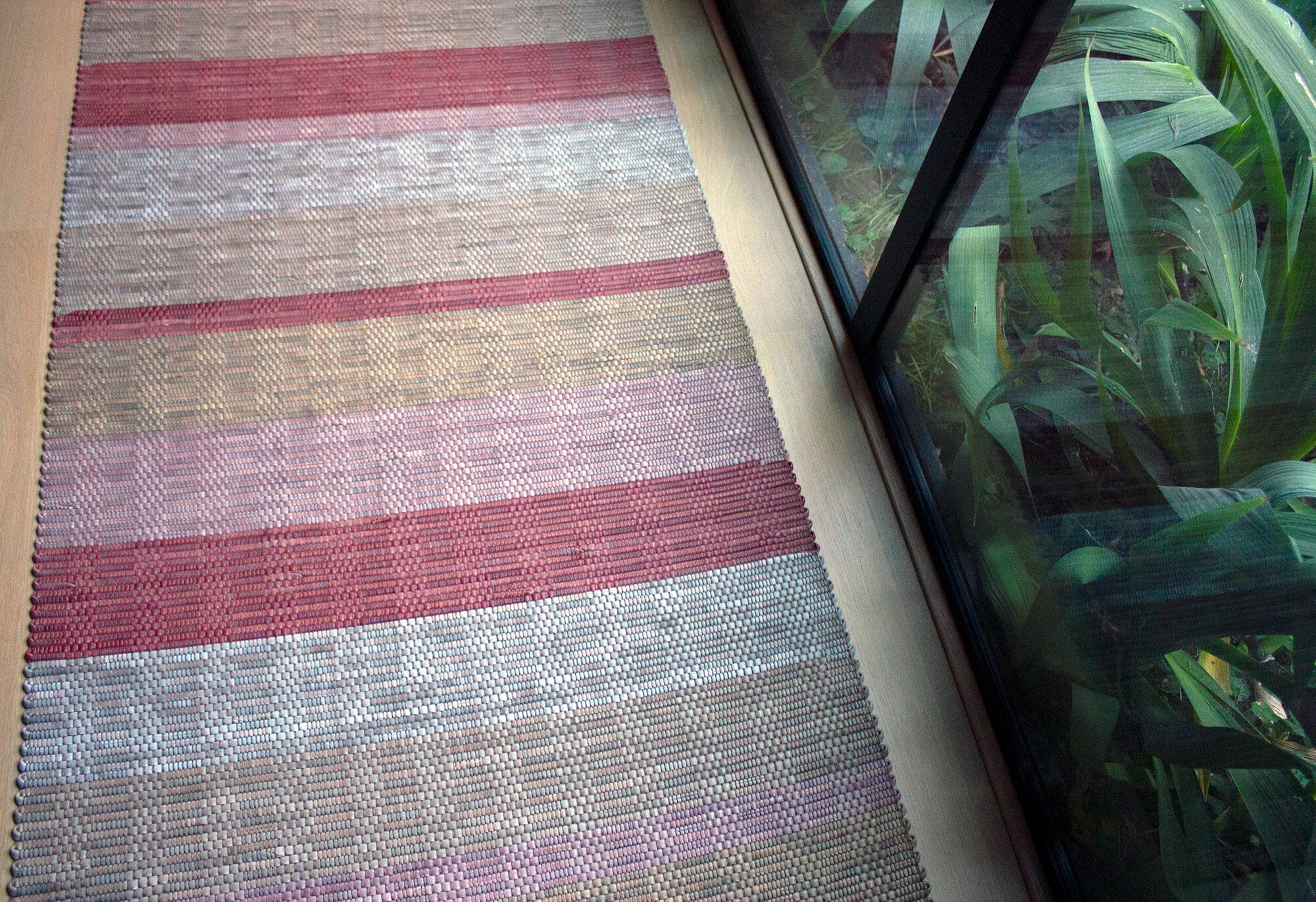 A woven leather floor rug in shades of purple and pink lays next to a large window.