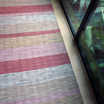 A woven leather floor rug in shades of purple and pink lays next to a large window.