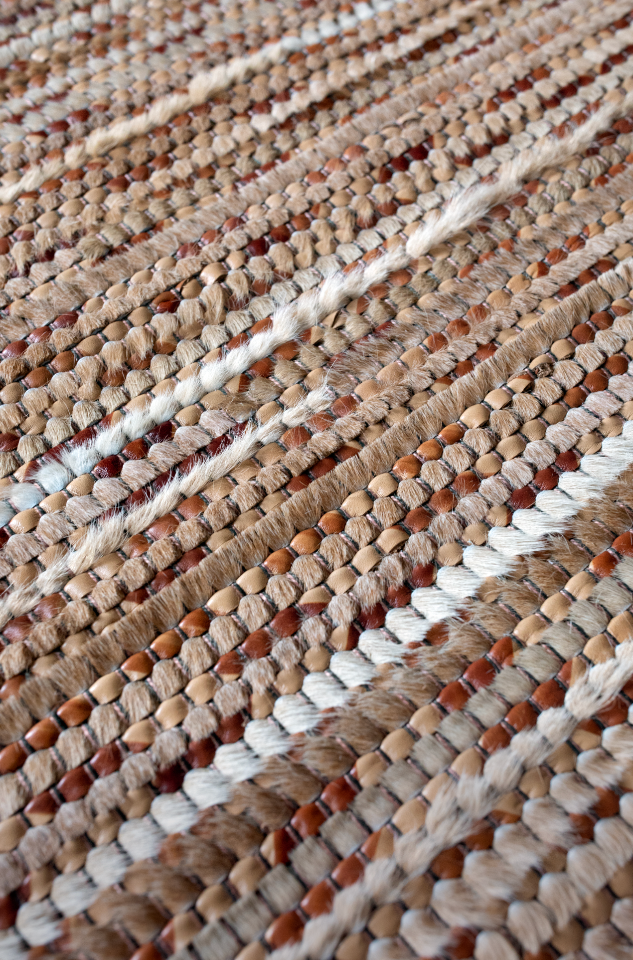 Detail of a woven leather rug in a striped grid texture in shades of brown and cream.