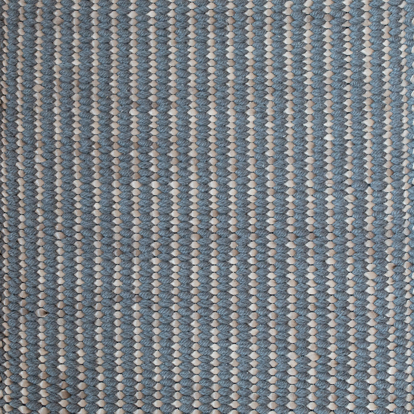 Detail of a woven leather rug in a gridded texture in blue with gray accents.