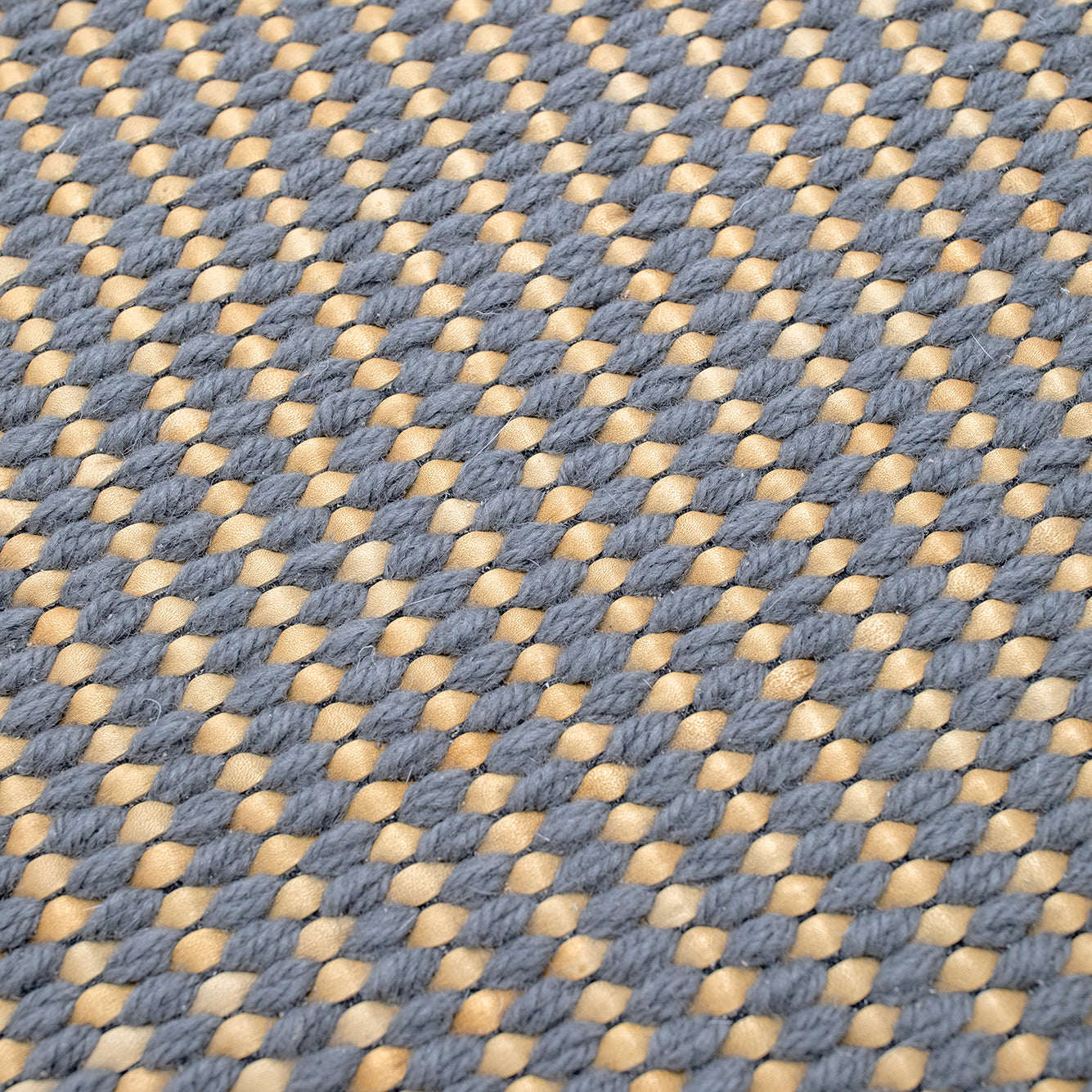 Detail of a woven leather rug in a gridded texture in gray with yellow accents.