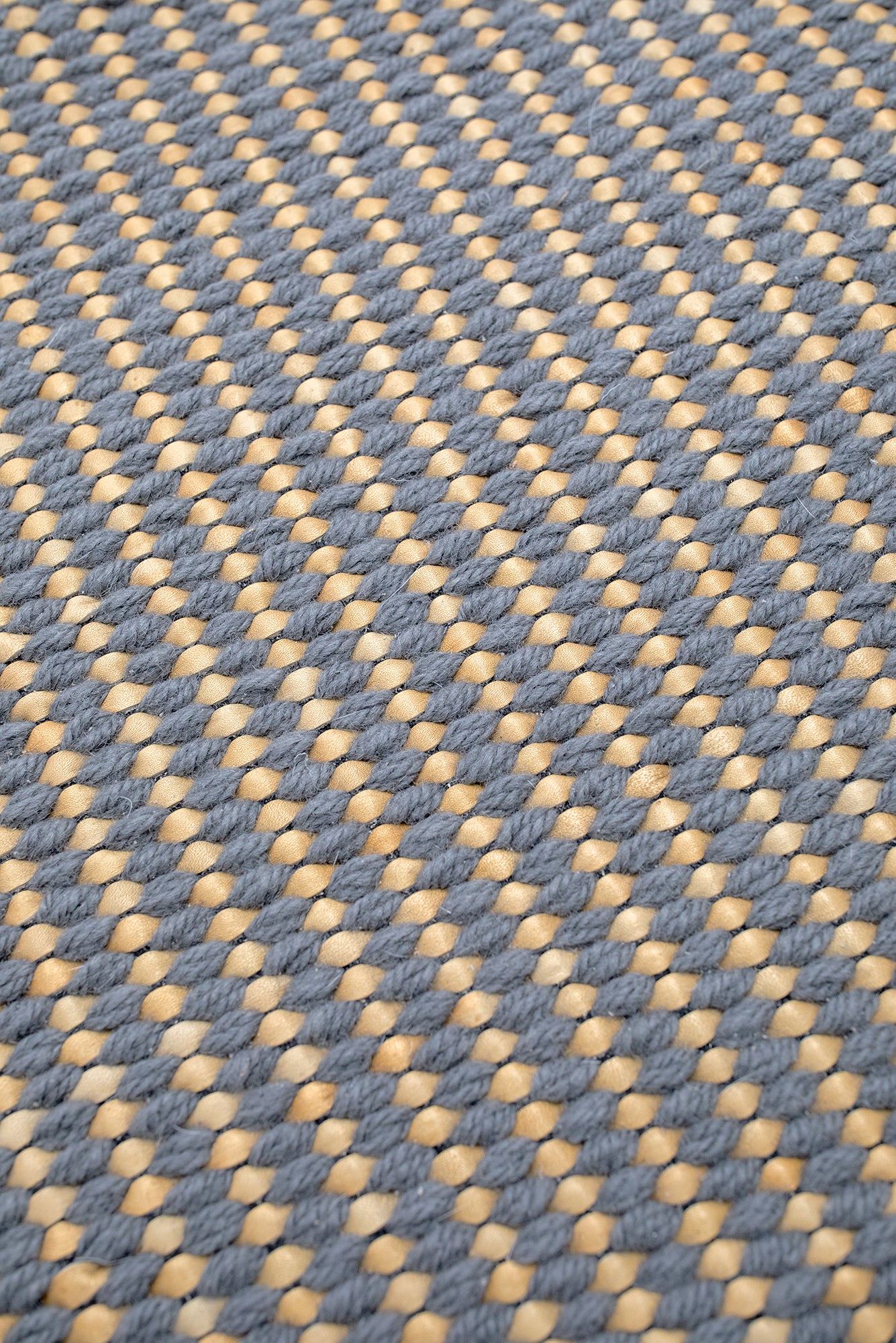 Detail of a woven leather rug in a gridded texture in gray with yellow accents.