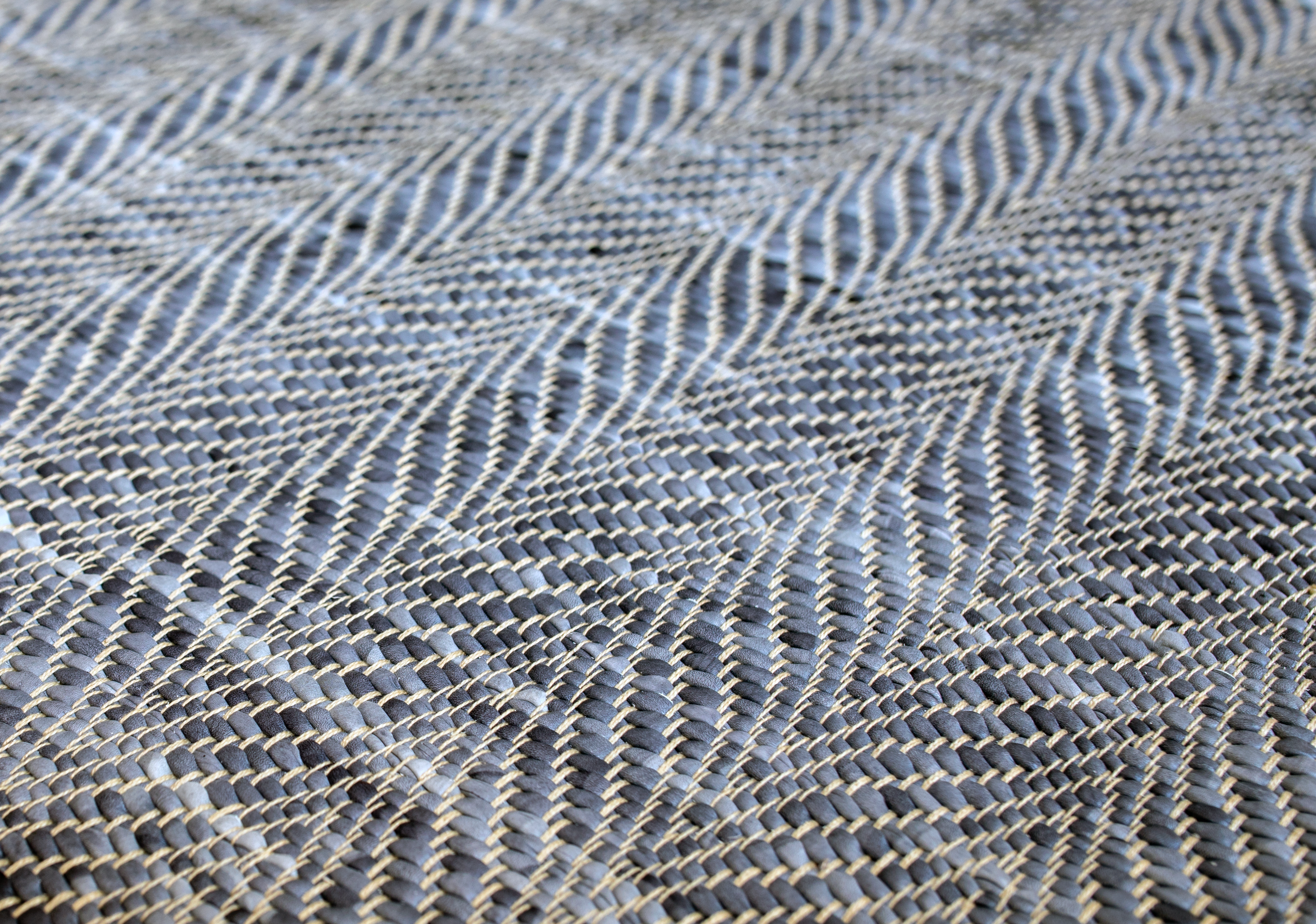 Detail of a woven leather rug in a striped wave texture in shades of blue with cream accents.