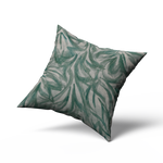 A throw pillow upholstered in cream leather with a painterly botanical overlay in green and gray.