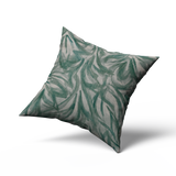 A throw pillow upholstered in cream leather with a painterly botanical overlay in green and gray.