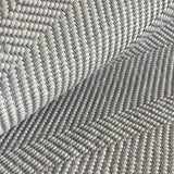 Detail of draped woven upholstery leather in a herringbone pattern in light gray.