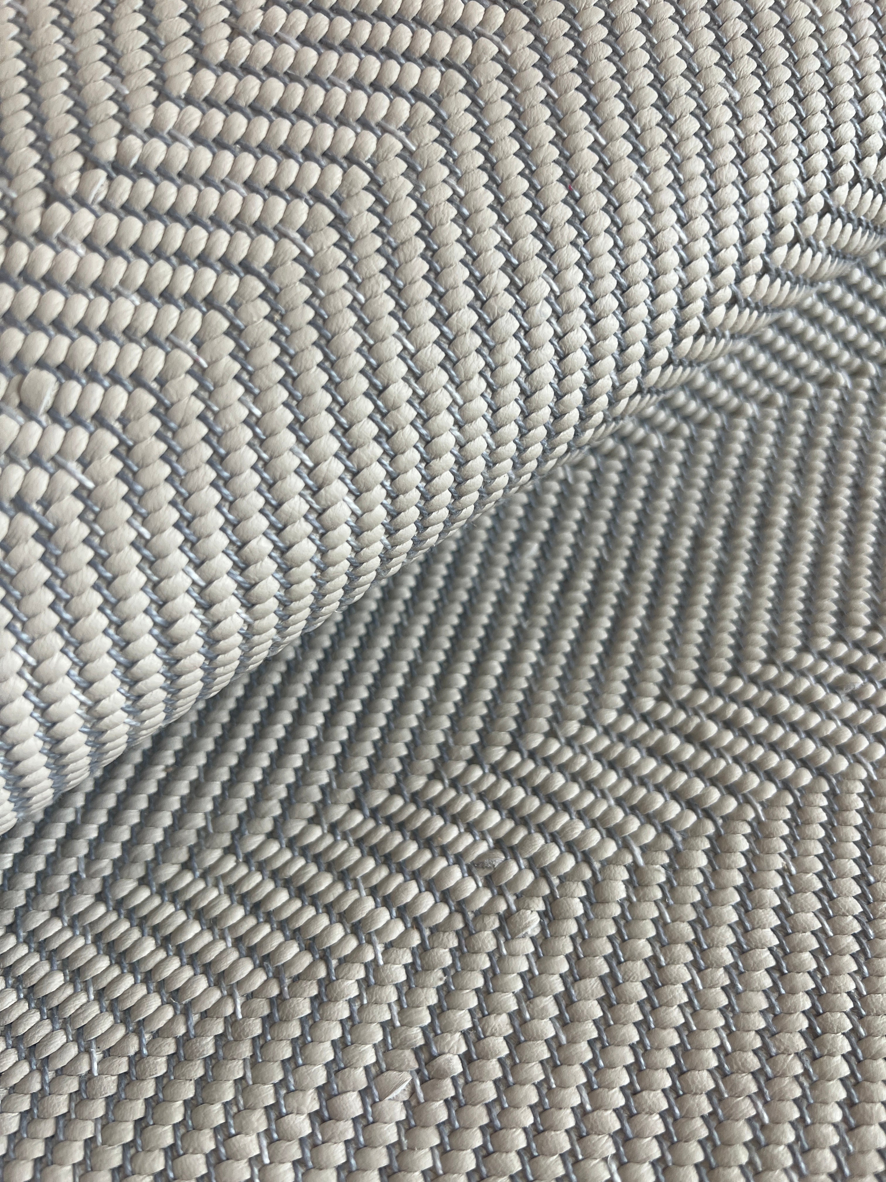 Detail of draped woven upholstery leather in a herringbone pattern in light gray.