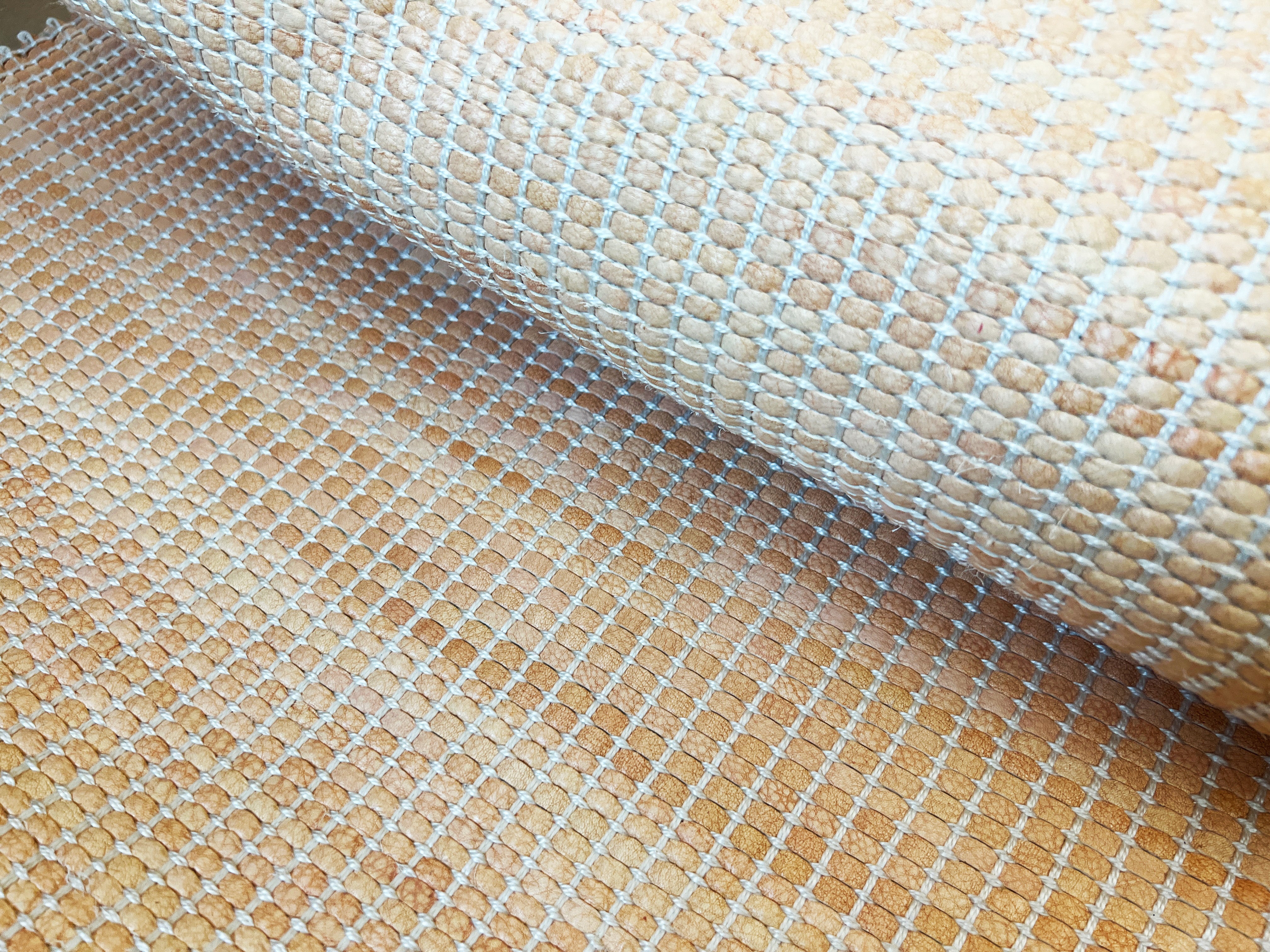 Draped upholstery leather yardage in a grid texture in mottled orange with white accents.