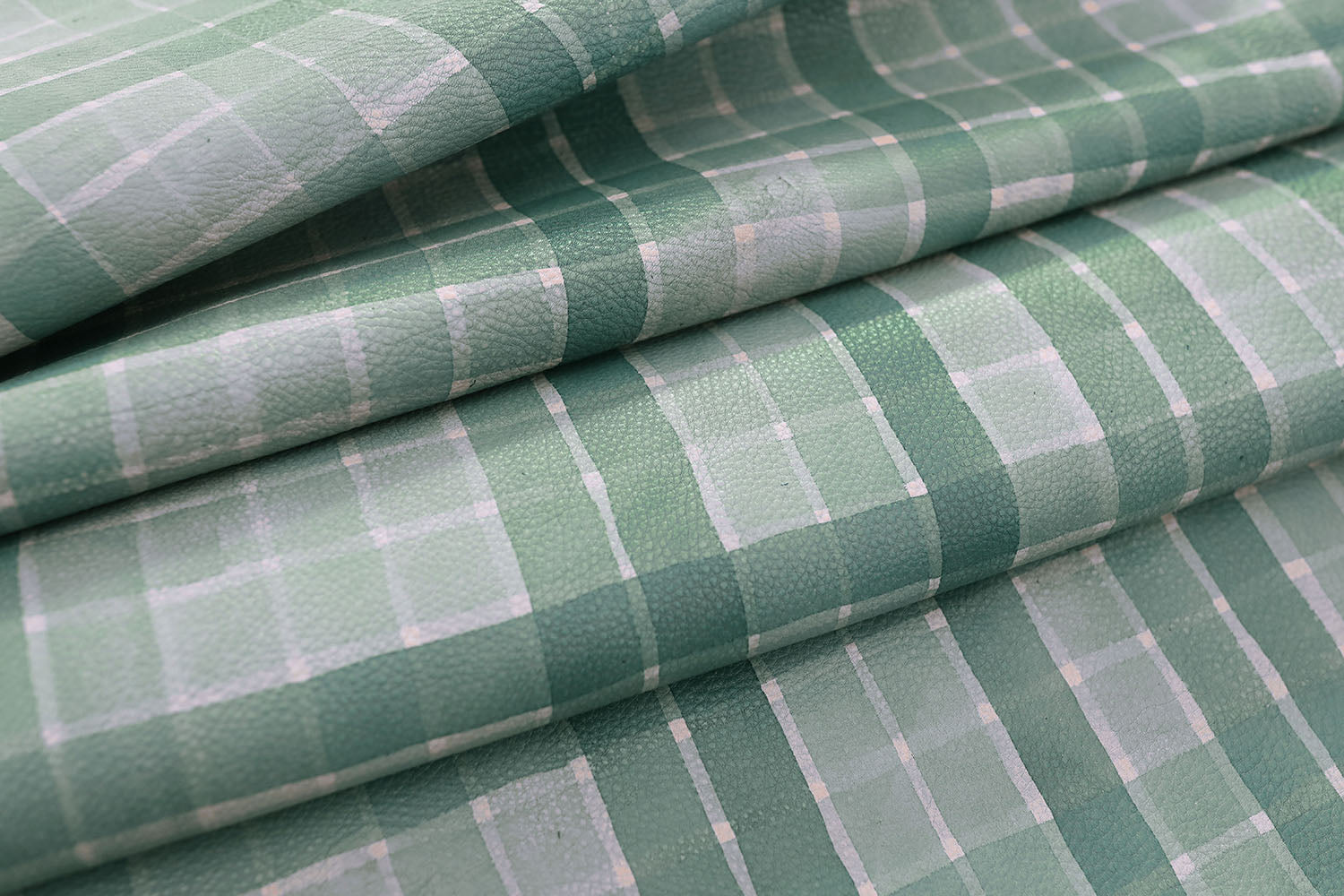 Detail of draped upholstery leather in a plaid pattern in shades of green and gray.