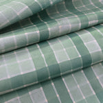 Detail of draped upholstery leather in a plaid pattern in shades of green and gray.