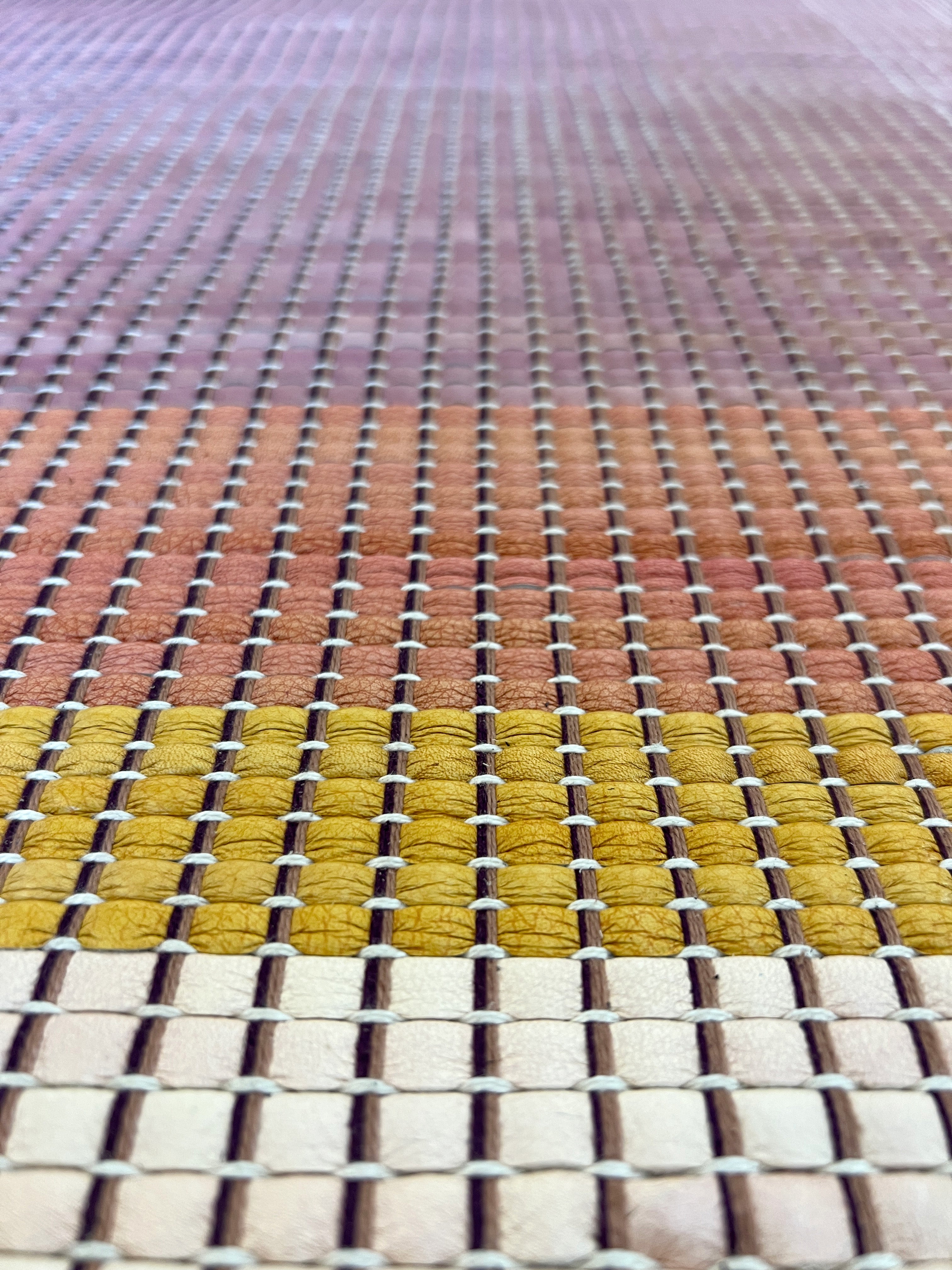 Close-up of a leather rug in a woven stripe pattern in shades of purple, black, coral and yellow.