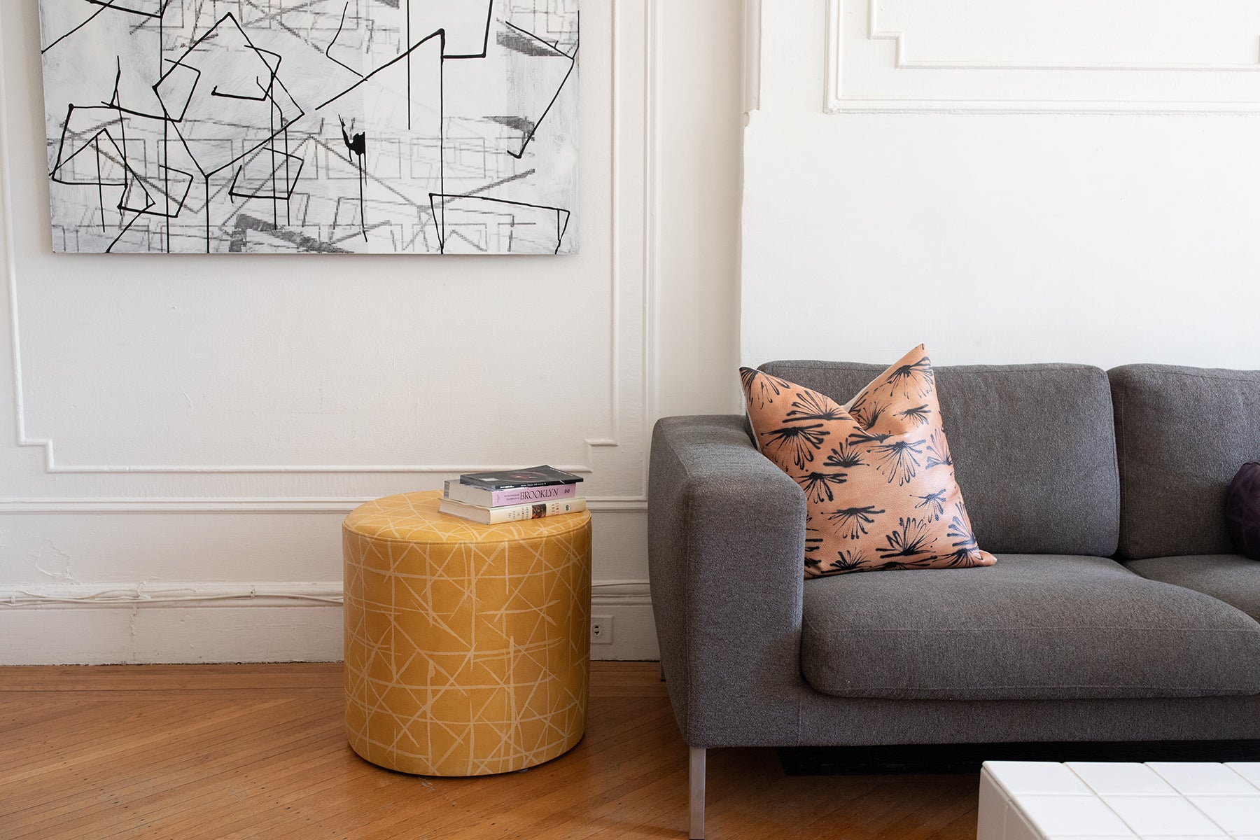 A living space with a round ottoman and throw pillow, both upholstered in patterned leather.