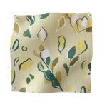 Square fabric swatch in a painterly leaf print in shades of green and yellow on a light yellow field.