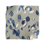 Square fabric swatch in a painterly leaf print in shades of white, blue and navy on a tan field.