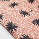 Partially unrolled fabric in a repeating palm tree print on a mottled field in shades of brown, gray, pink and white.