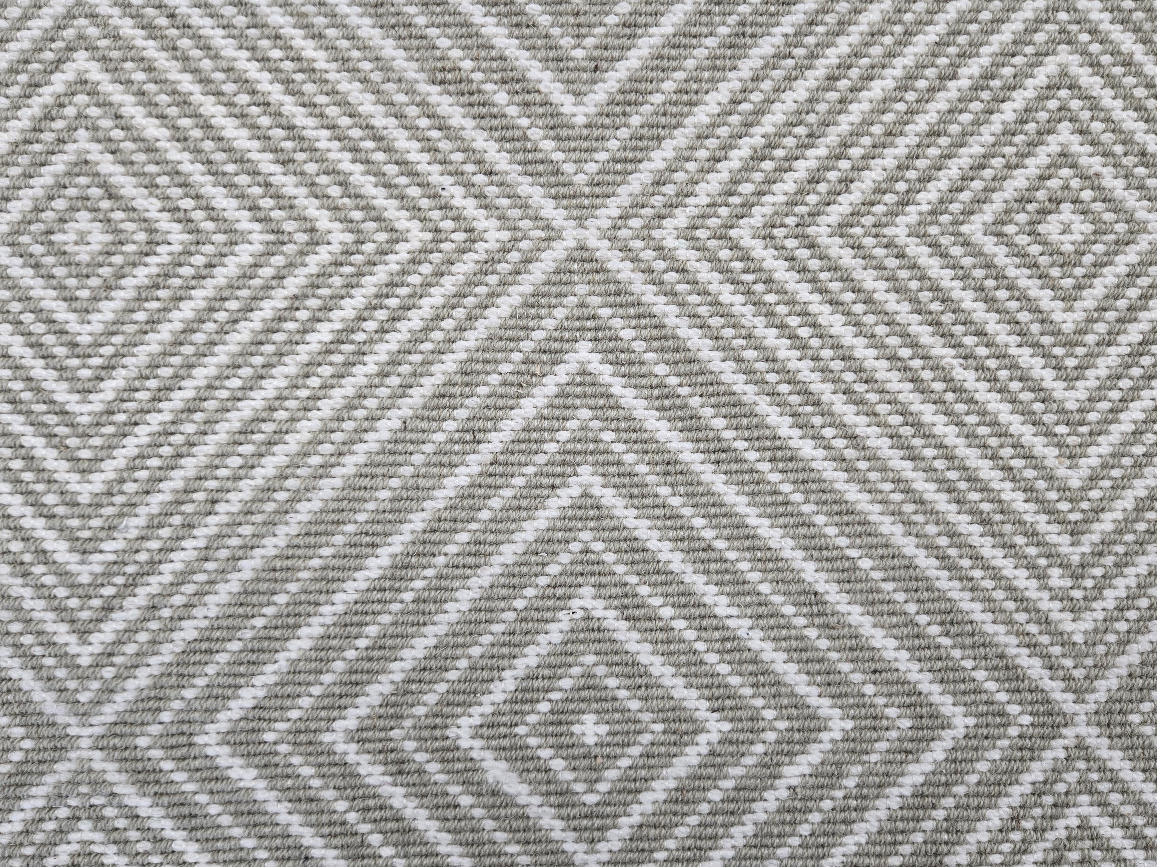 Broadloom carpet sample in a linear diamond design in white and green-grey.