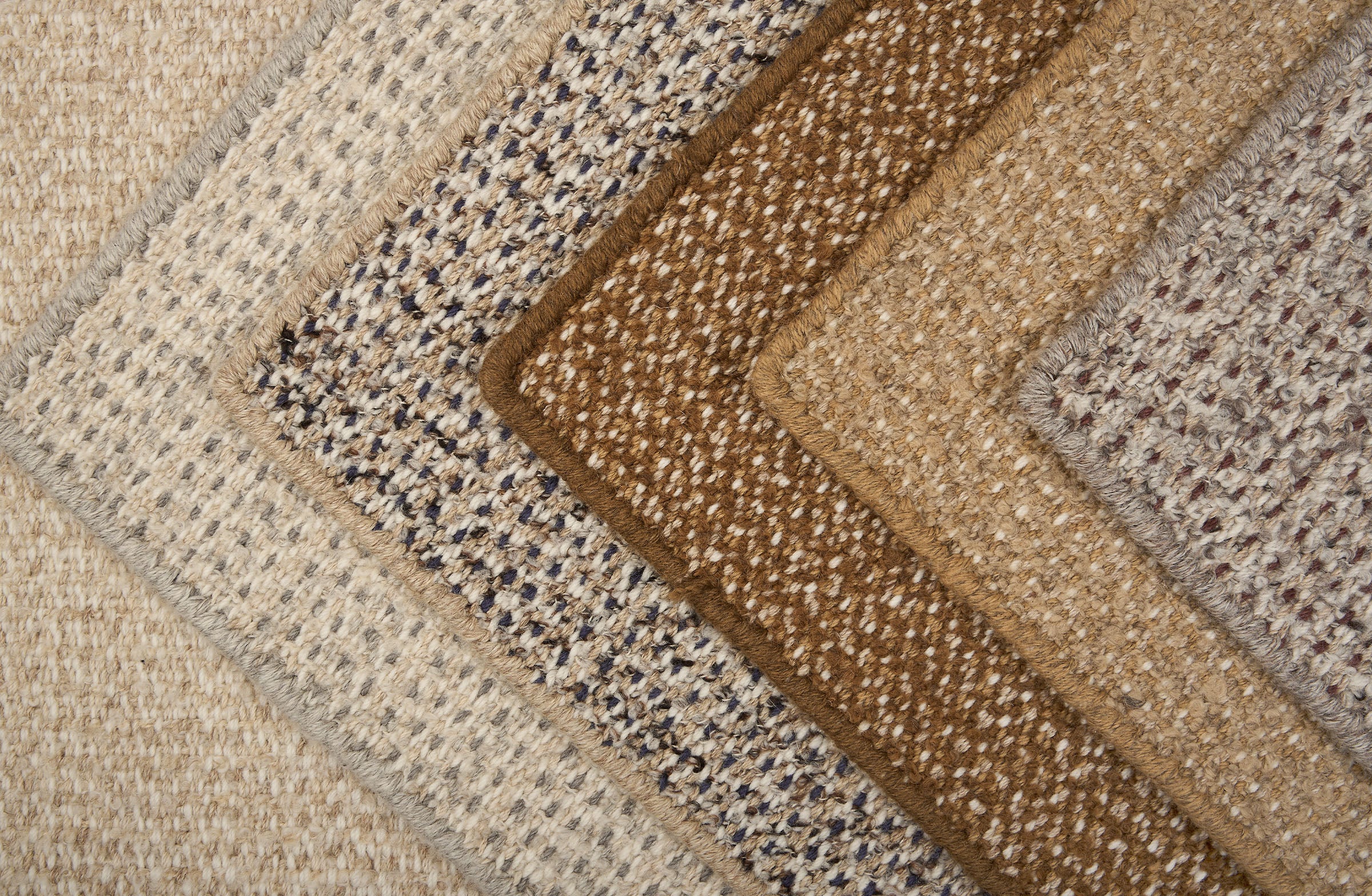 Stack of broadloom carpets in a textural weave in shades of taupe, cream, brown , blue and grey.