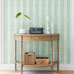 A styled end table stands in front of a wall papered in a geometric stripe print in green, turquoise and cream.