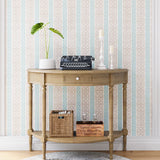 A styled end table stands in front of a wall papered in a geometric stripe print in blue, tan and cream.
