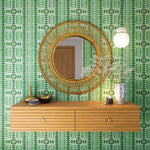 A floating shelf and statement mirror hang on a wall papered in a geometric stripe print in shades of green and purple.