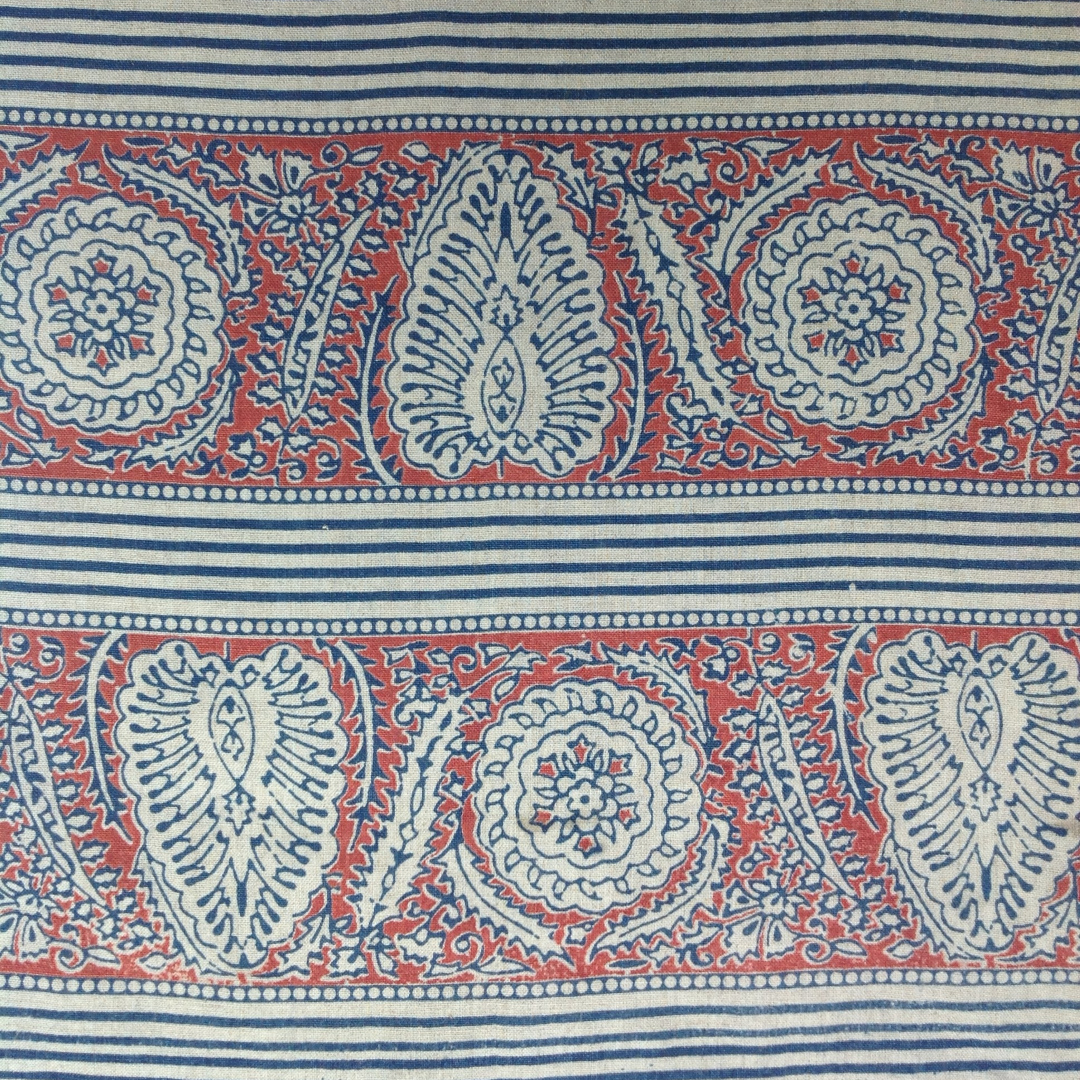 Block printed fabric in an ornamental paisley stripe in indigo and red on linen.