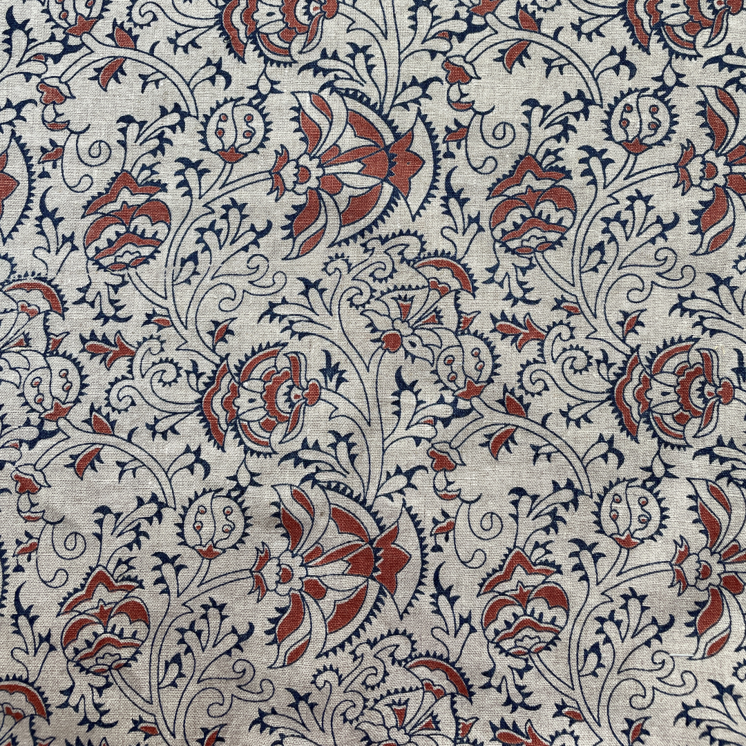 Handprinted fabric in a scrolling floral paisley in indigo with red accents on natural linen