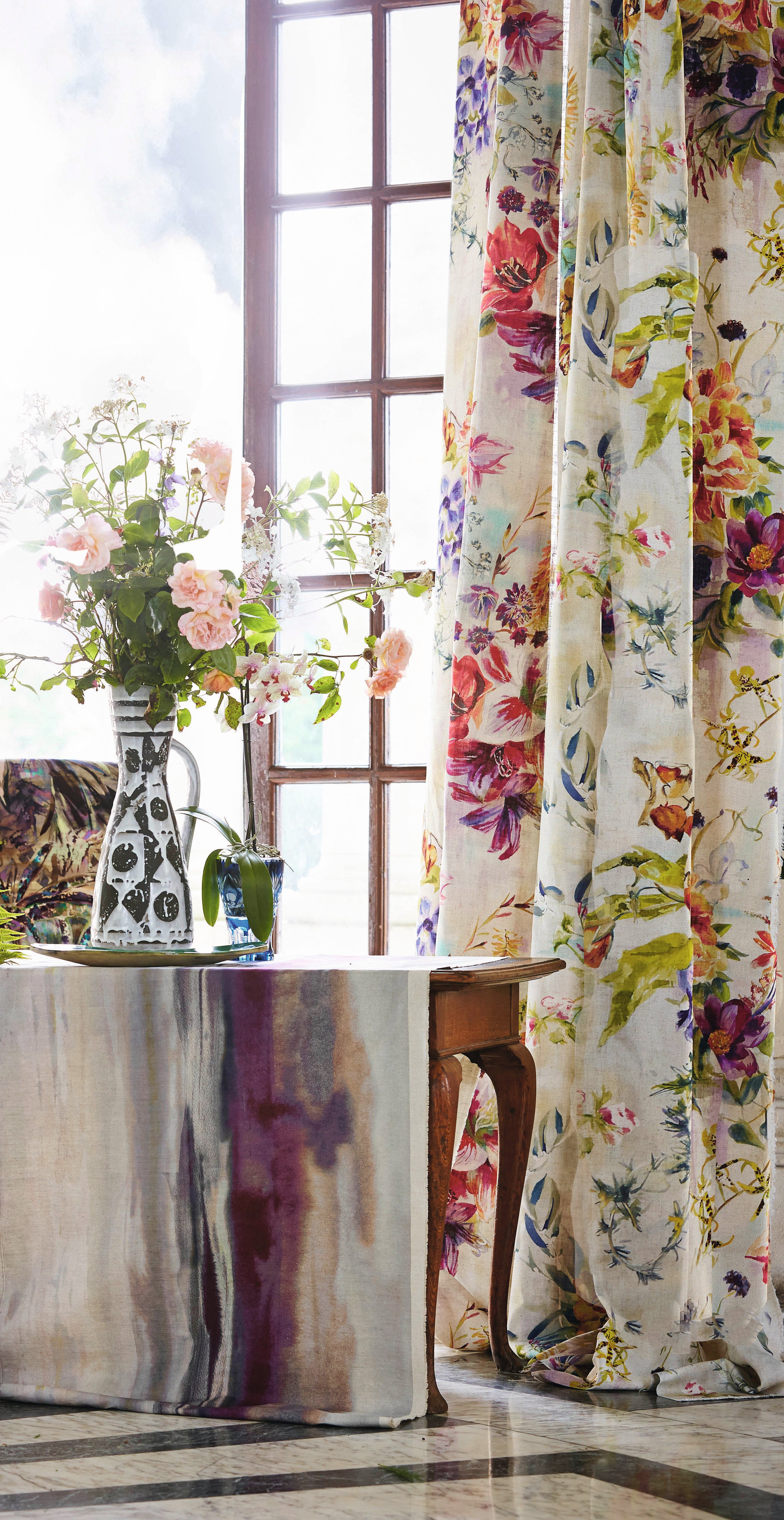 A sunny dining room tableau with a large window and curtains in a painterly floral print.