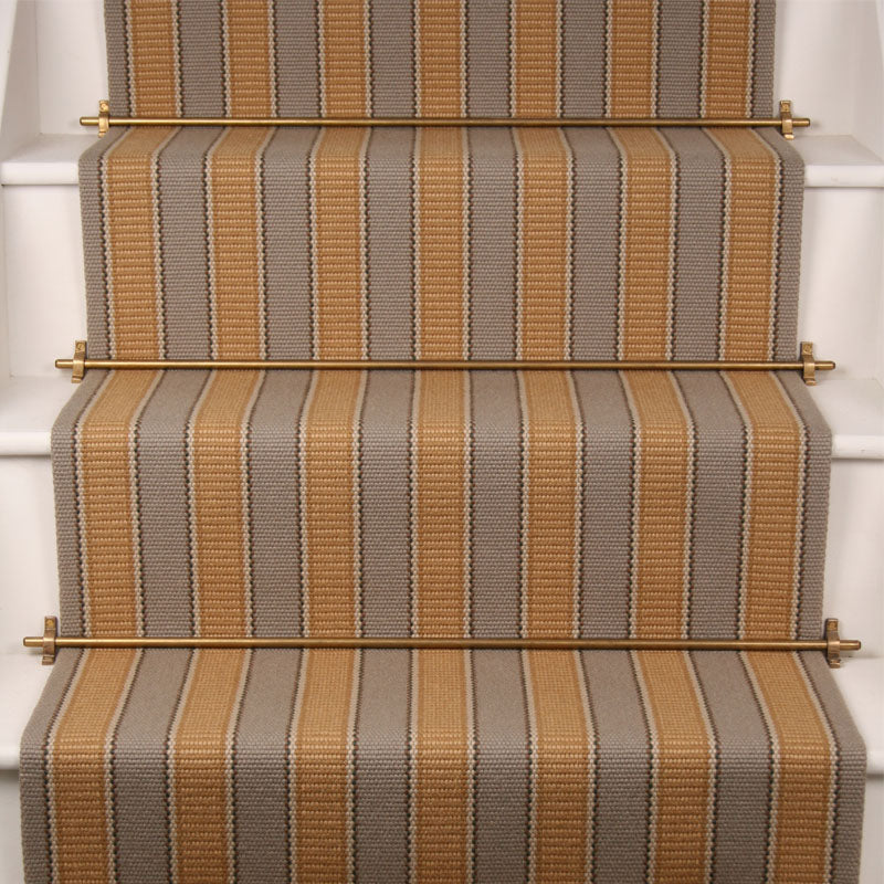 Striped flatweave runner in taupe and mustard yellow installed on white stairs.