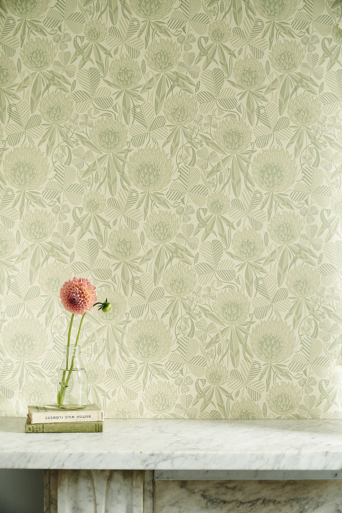 Wallpaper in sage green botanical design of clover flowers and leaves, with a marble shelf with a pink flower and books