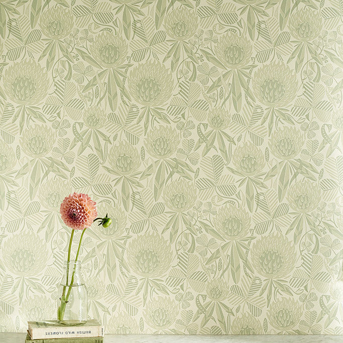 Wallpaper in sage green botanical design of clover flowers and leaves, with a marble shelf with a pink flower and books