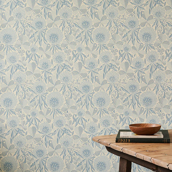 Wallpaper in a a blue tonal botanical design of clover flowers and leaves, with wooden table with props.