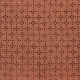Detail of fabric in a geometric lattice print in brown on a burnt orange field.