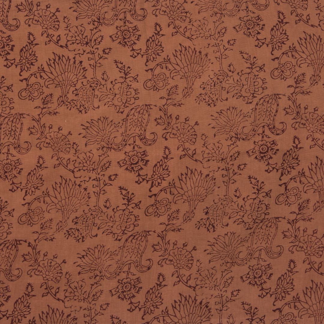 Detail of fabric in a paisley print in brown on a burnt orange field.