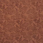 Detail of fabric in a paisley print in brown on a burnt orange field.