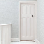 A door stands at the end of a hallway papered in a dense herringbone print in light gray on a white field.