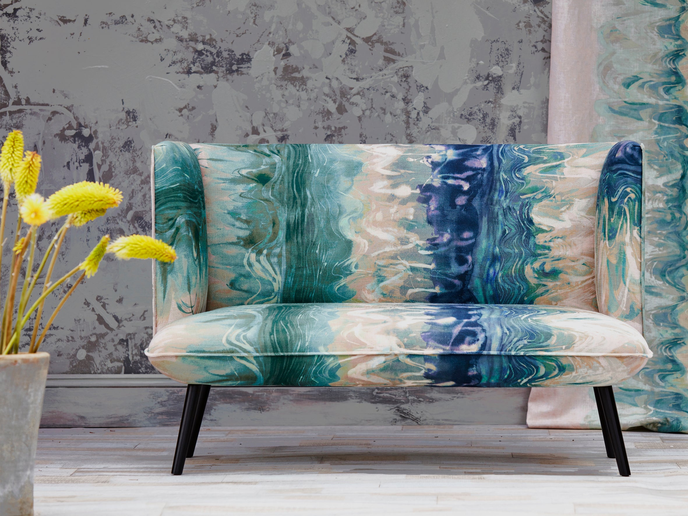 A loveseat upholstered in an abstract paint blot pattern in shades of green, navy and blue on a mottled cream field.