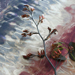 A sprig of flowers lays on top of fabric yardage in an absract paint blot print in shades of red, navy and cream.