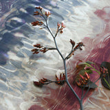 A sprig of flowers lays on top of fabric yardage in an absract paint blot print in shades of red, navy and cream.