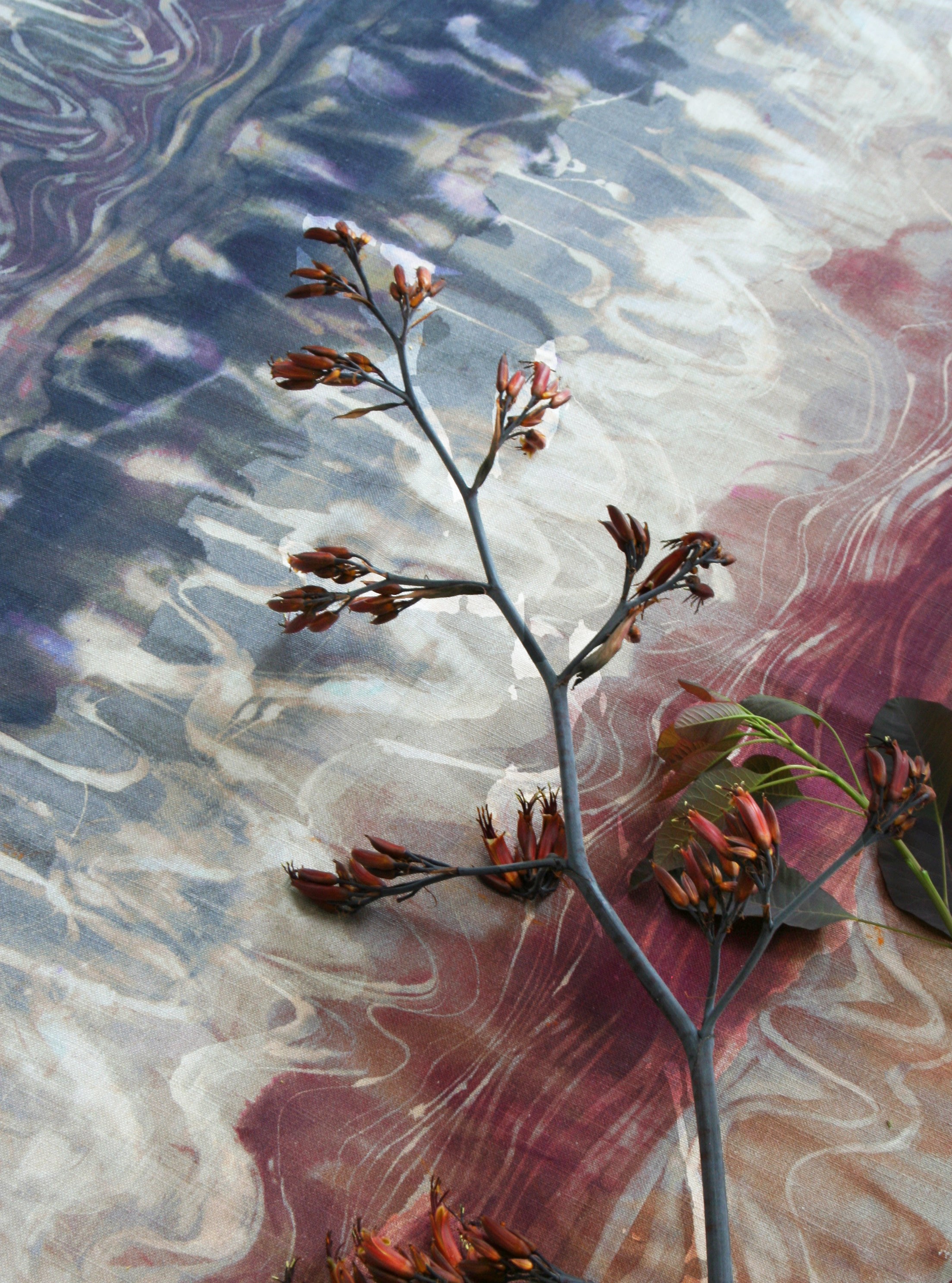 A sprig of flowers lays on top of fabric yardage in an absract paint blot print in shades of red, navy and cream.