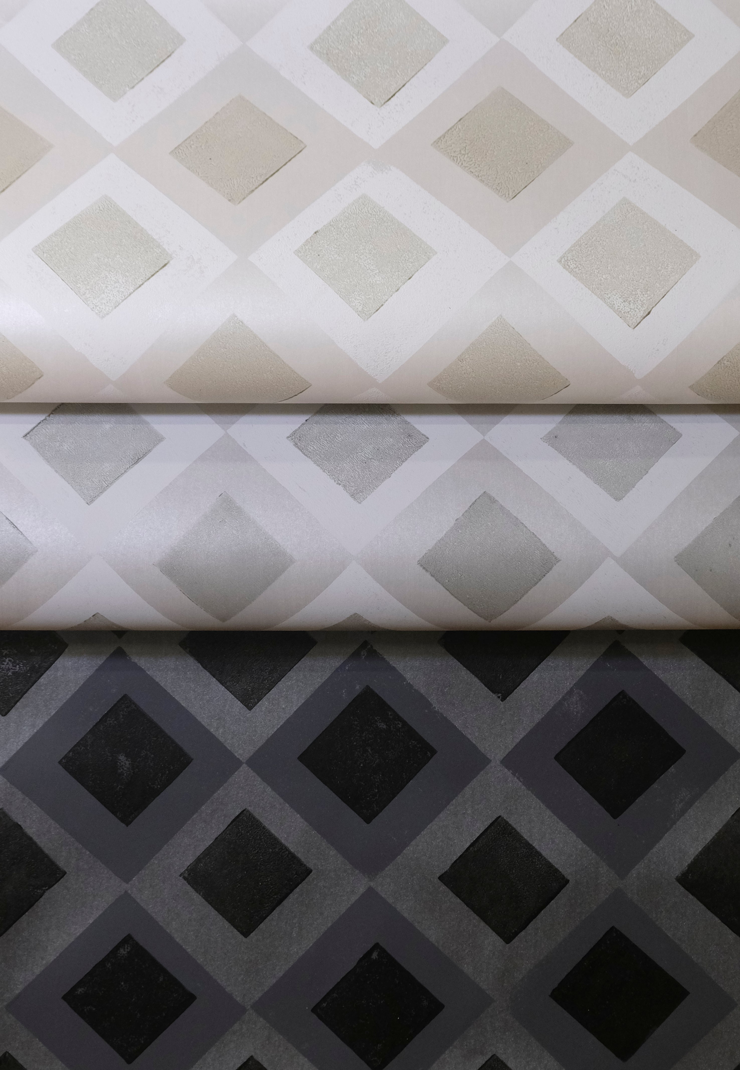 Three rolled pieces of wallpaper in different neutral colorways of a diamond lattice print.