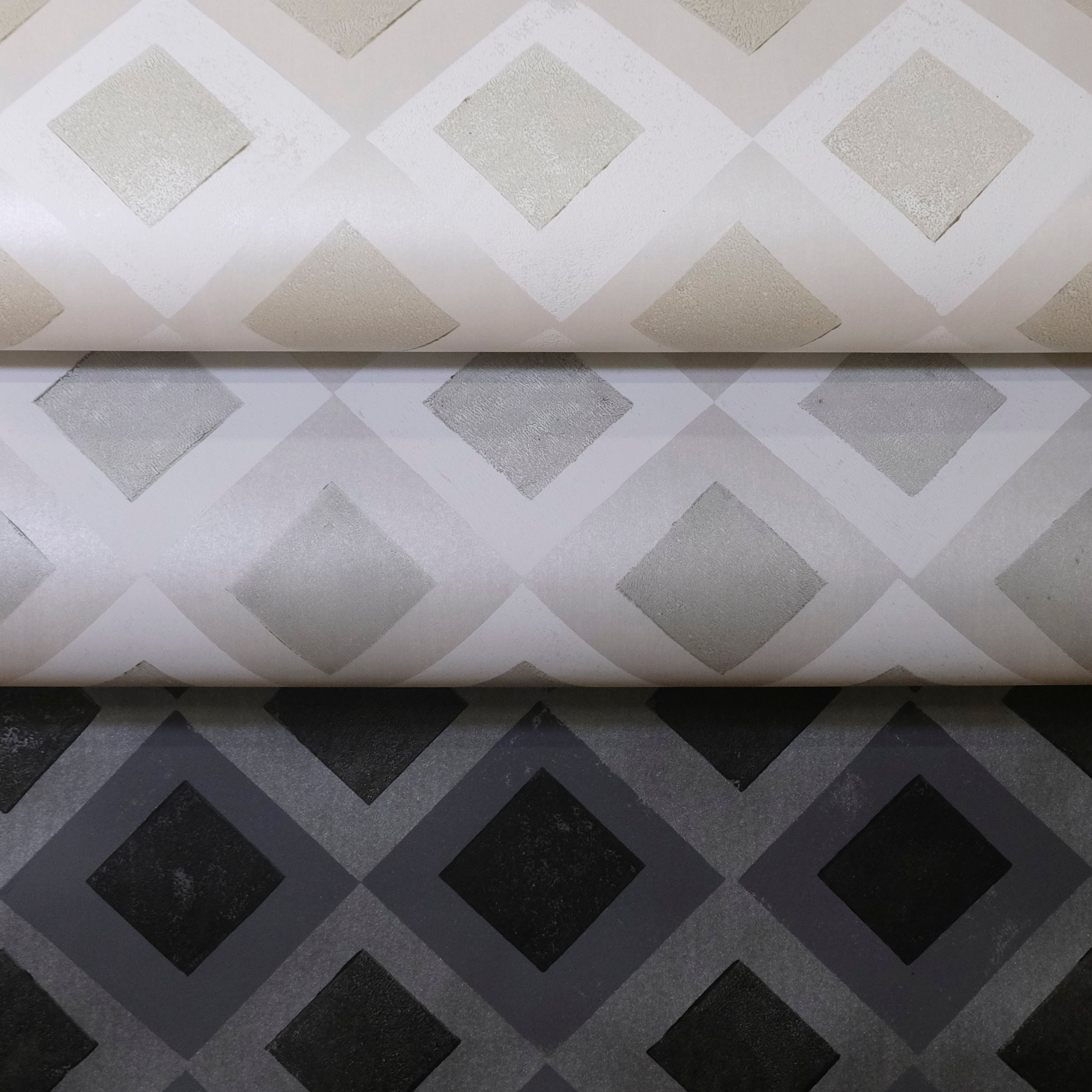 Three rolled pieces of wallpaper in different neutral colorways of a diamond lattice print.