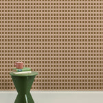 A green wooden stool with books and a mug against a wallpapered wall in a gridded check pattern in brown, cream and mauve. 